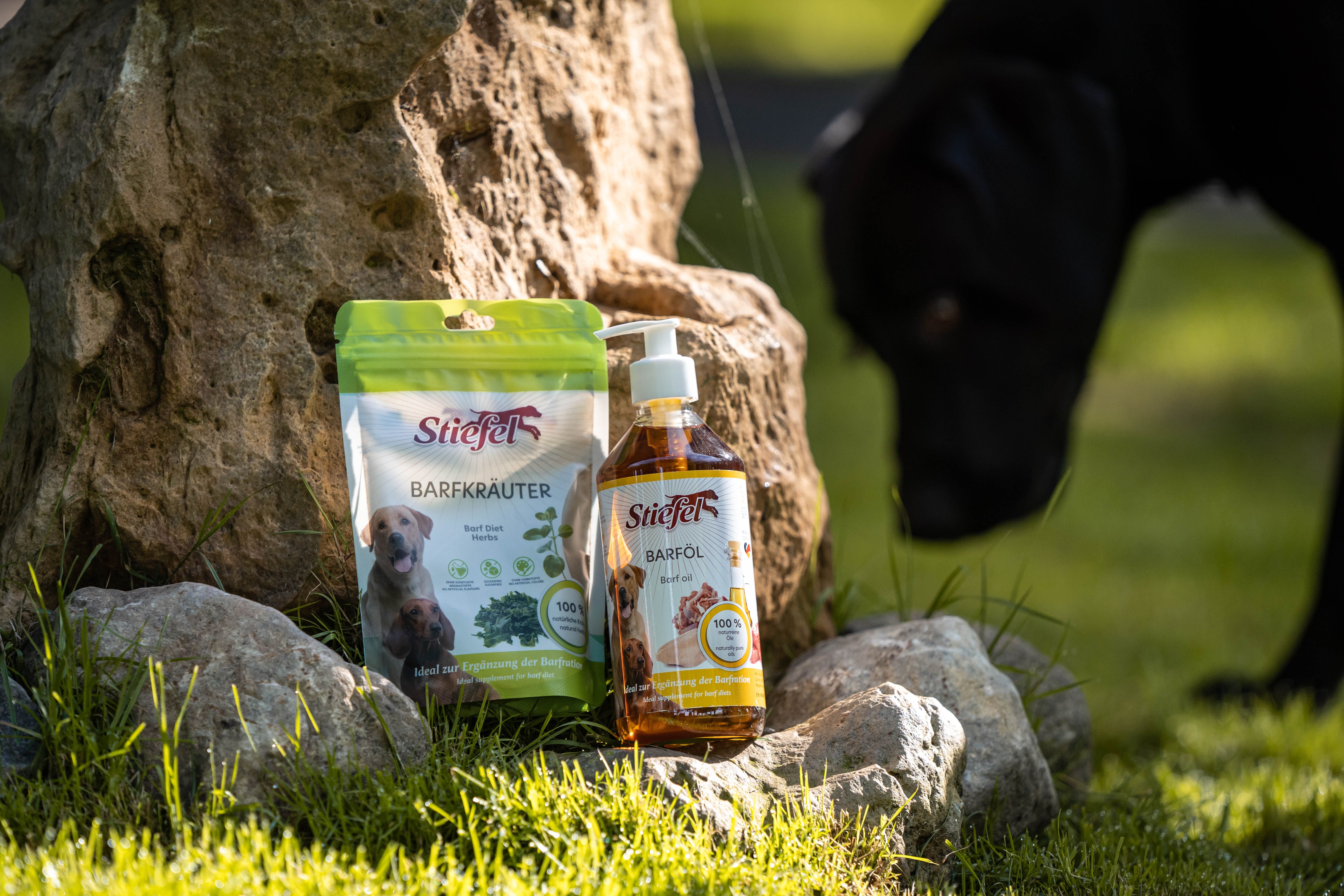 Barföl-Flasche und Barfkräuter-Beutel neben Steinen. Hund im Hintergrund.