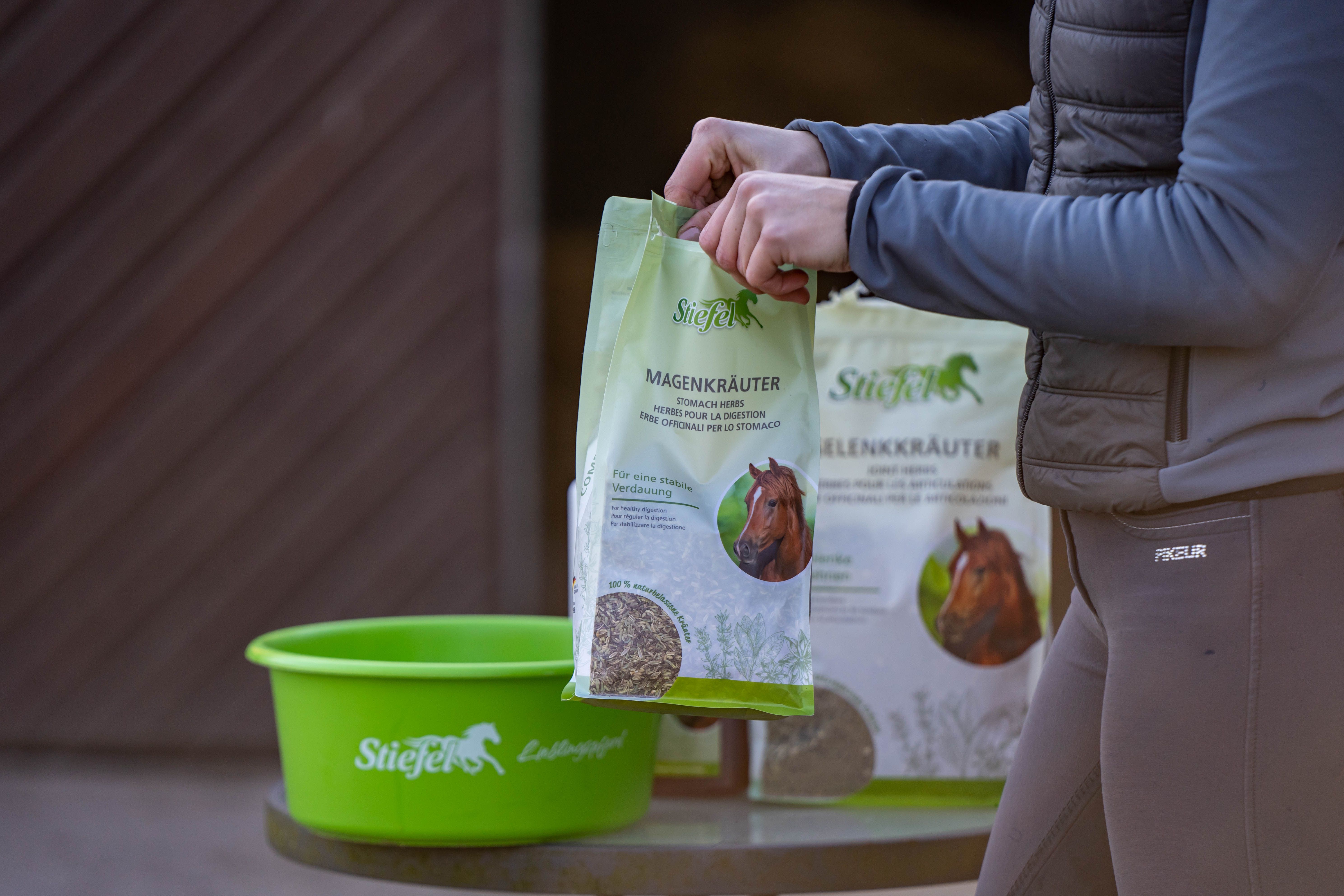 Person hält eine grüne Tüte Stiefel Magenkräuter. Neben einem grünen Behälter. Produktverpackung.