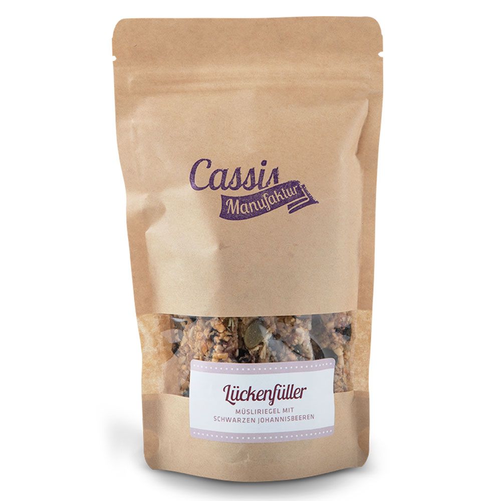 Beutel mit Müsli-Riegeln. Sichtbares Etikett mit "Lückenfüller mit schwarzen Johannisbeeren". Logo "Cassis Manufaktur".