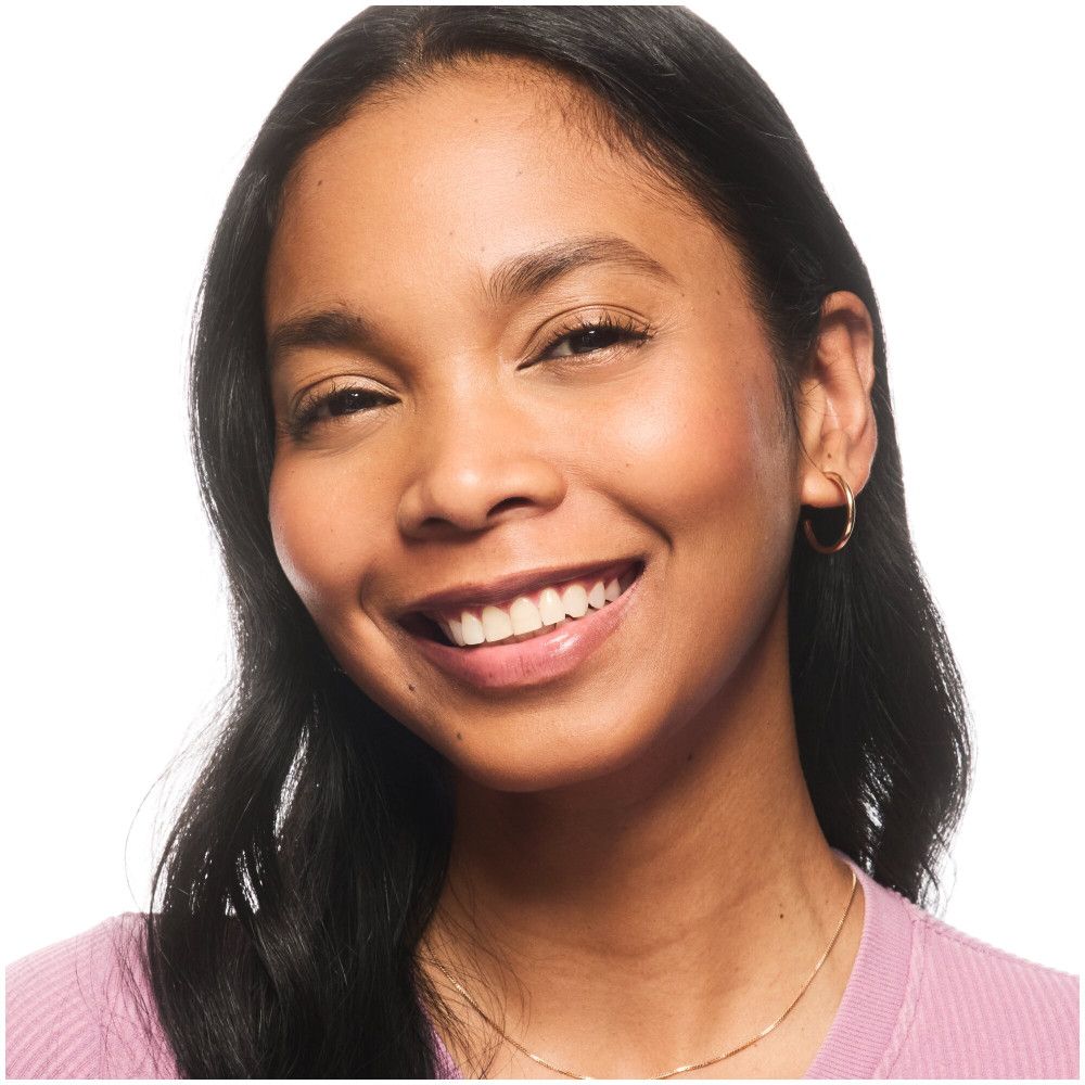 Porträt einer lächelnden Frau. Sie trägt Foundation und hat einen ebenmäßigen Teint. Goldene Creolen.