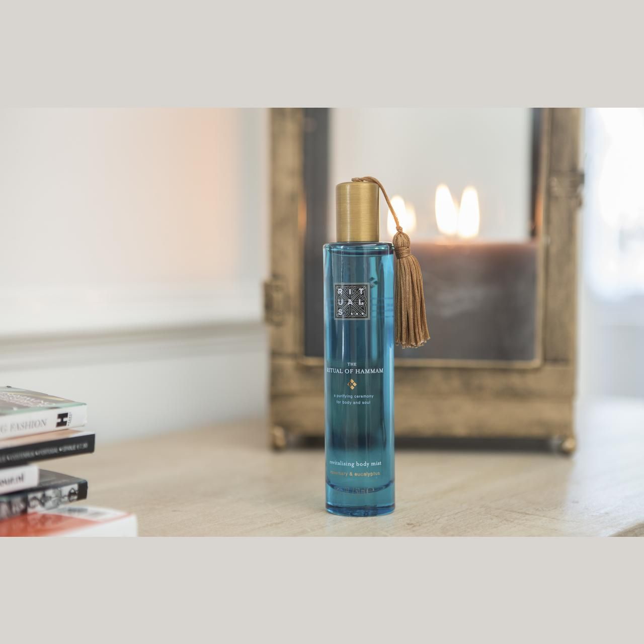 Türkisgrüne Flasche mit goldfarbenem Deckel und Quaste. Aufschrift: Rituals, The Ritual of Hammam, Revitalizing Body Mist. Auf Tisch.