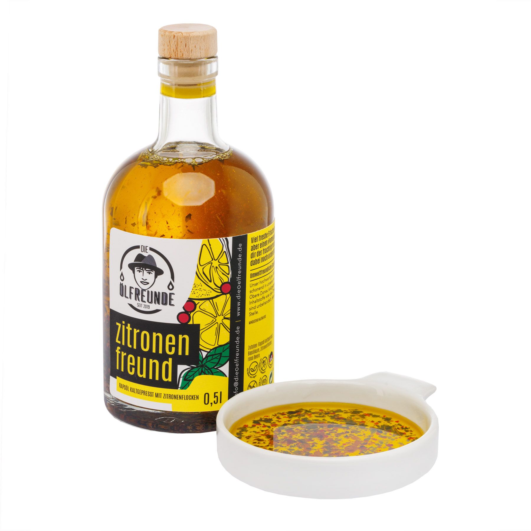 Glasflasche mit Korken und Flüssigkeit, daneben eine kleine Schale mit Flüssigkeit. Etikett mit Produktname.