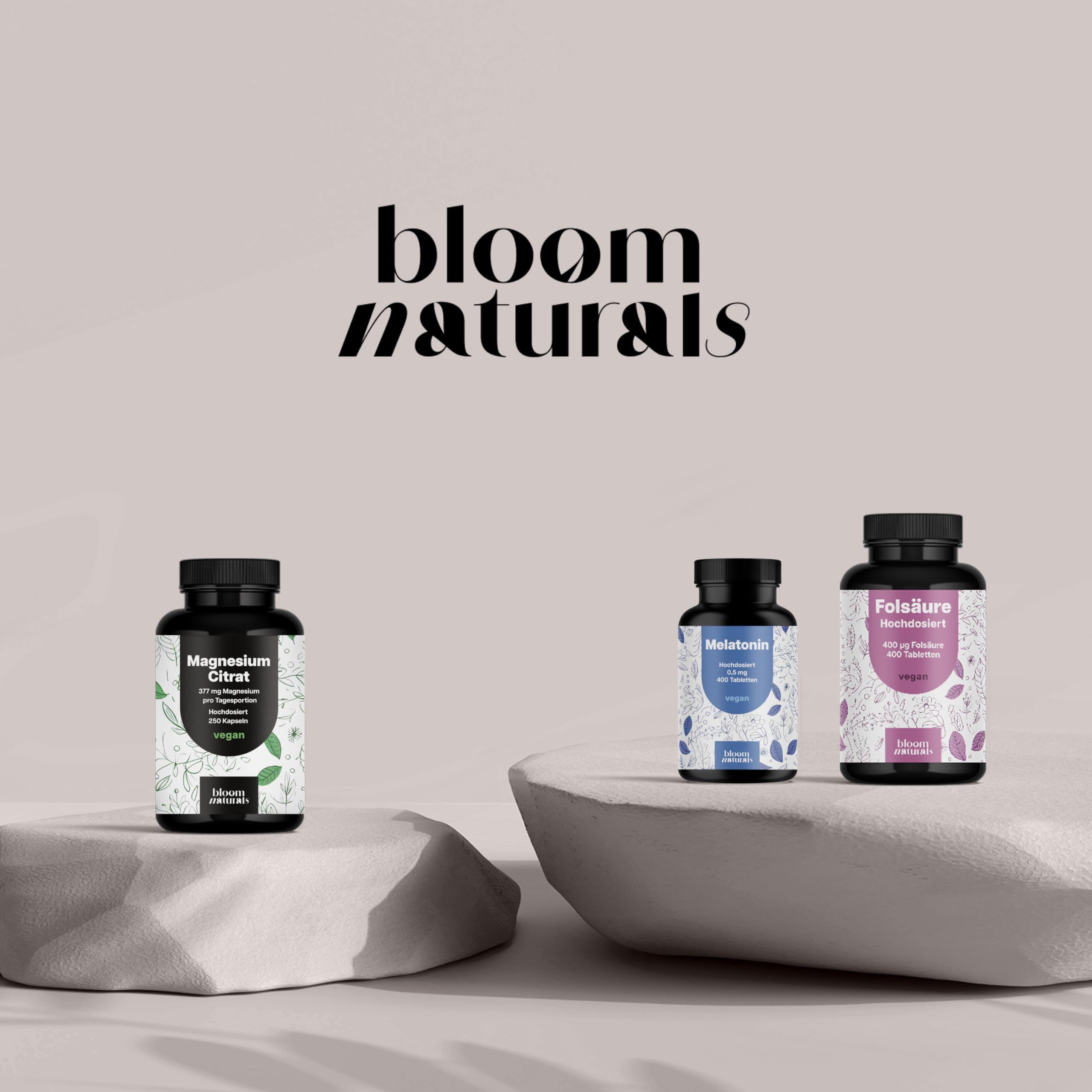 Drei Bloom Naturals Flaschen auf Steinen: Magnesium Citrat, Melatonin, Folsäure. Minimalistisches Design.