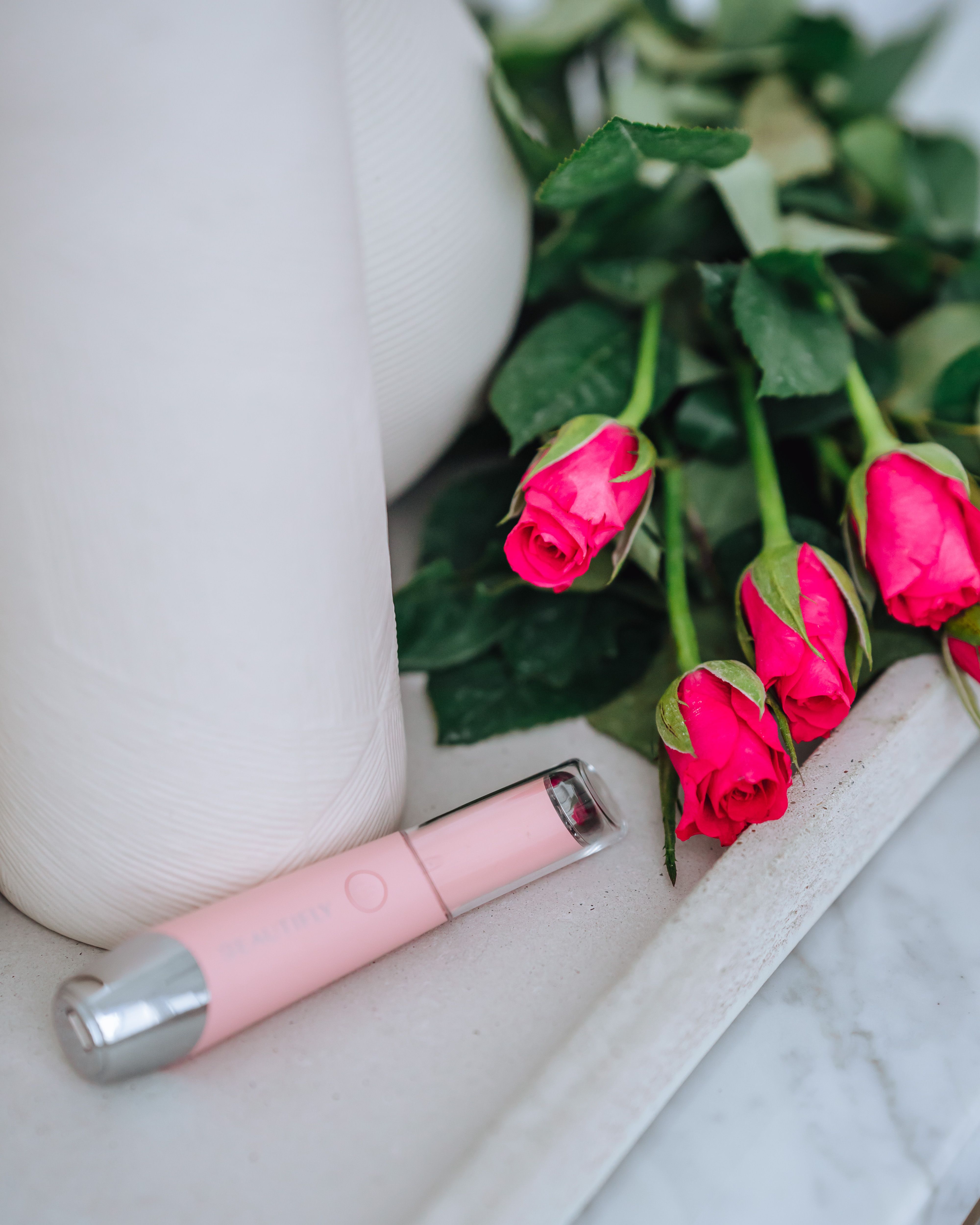 Rosa Gerät mit silbernen Enden neben Rosen und Vase. LED-Lichttherapiegerät.
