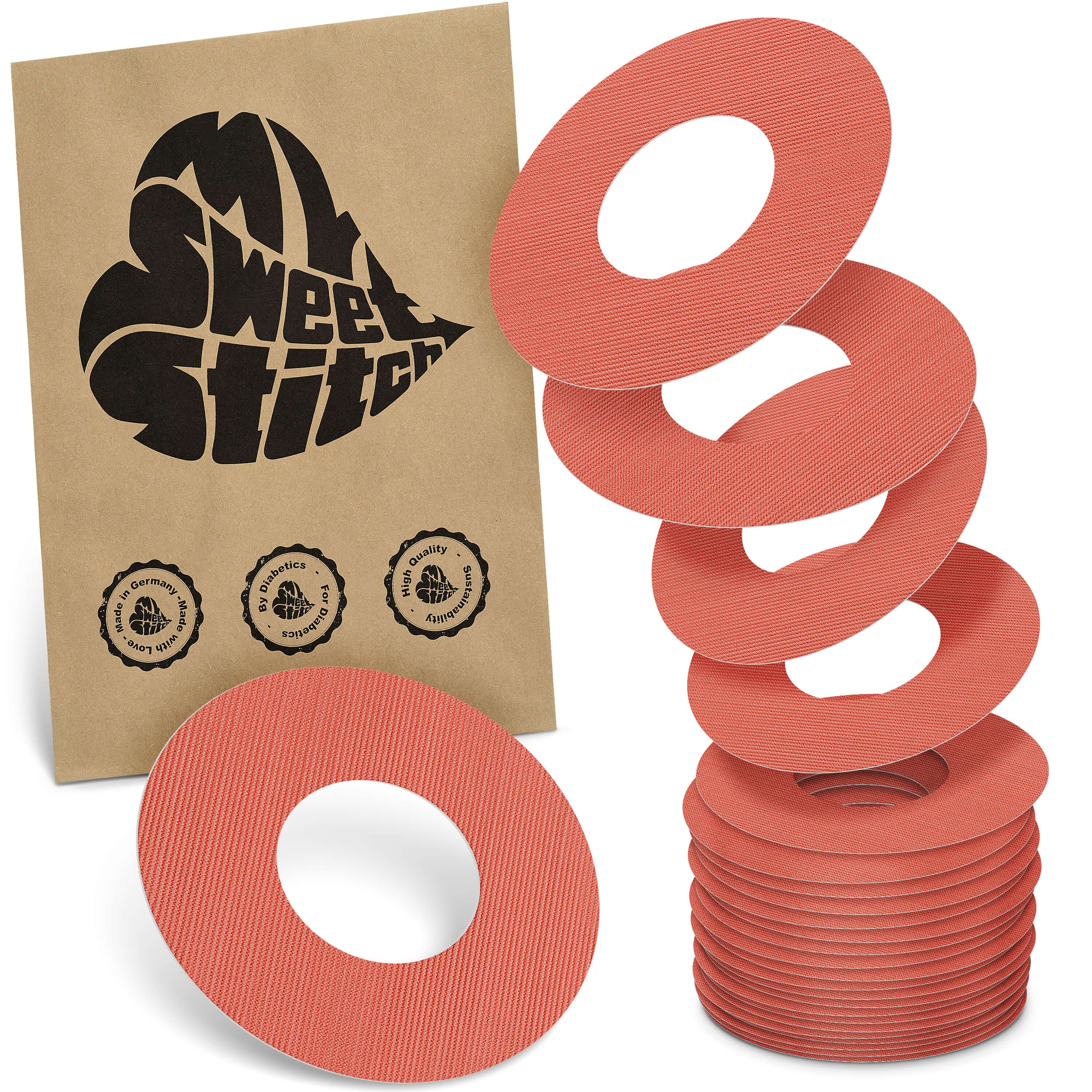 Runde, rosafarbene Ringpflaster. Auf einem Stapel und lose daneben. Braune Verpackung mit Logo und Siegeln.