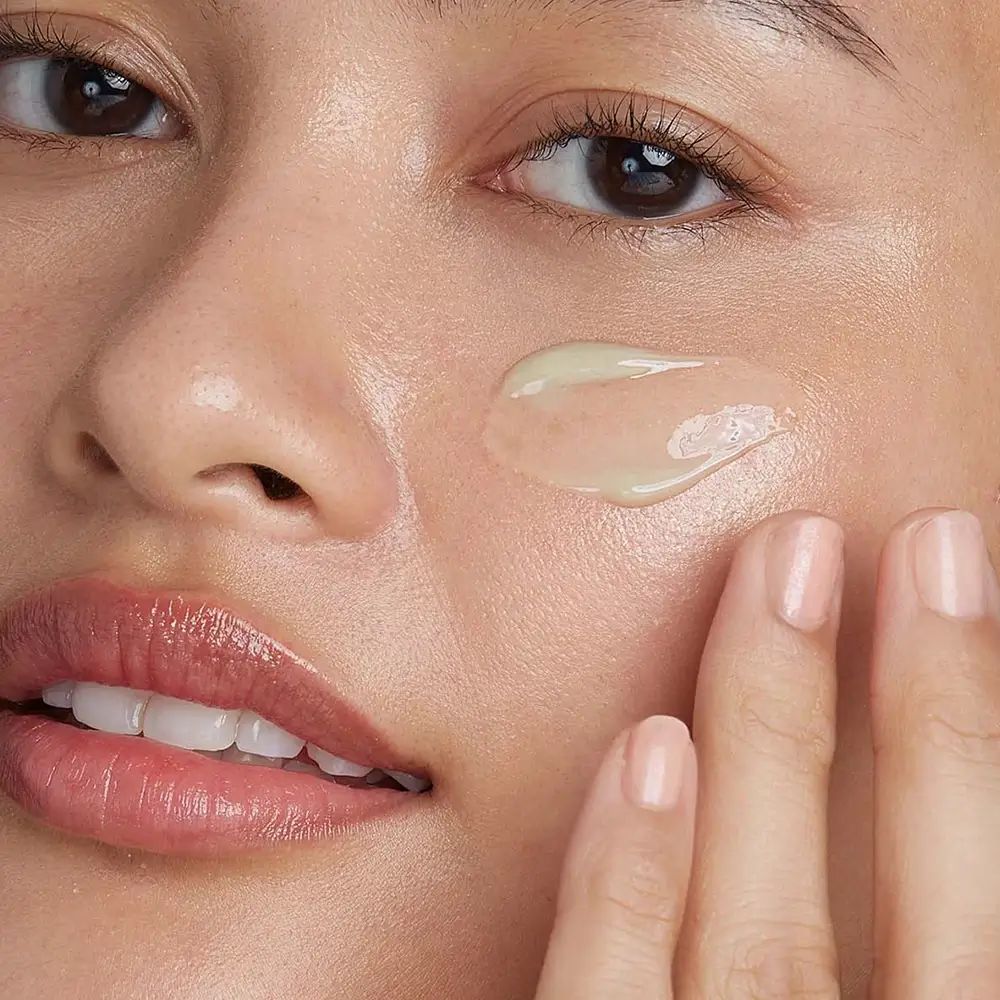 Nahaufnahme einer Person, die ein Produkt auf ihr Gesicht aufträgt. Gelbliche Creme wird auf die Haut aufgetragen.