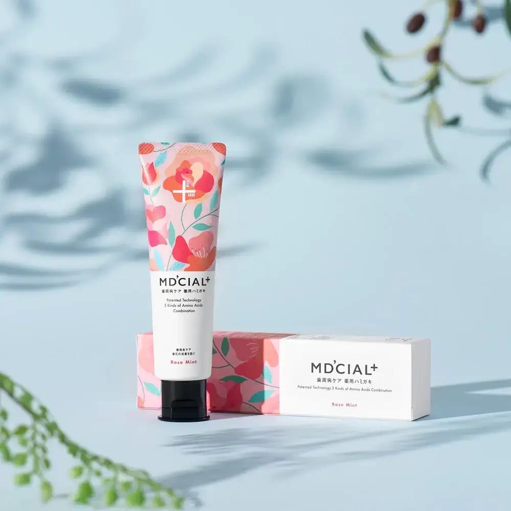 Zahnpasta-Tube, MD'CIAL+, Rose Mint, mit Schachtel. Floral bedruckt. Blauer Hintergrund.