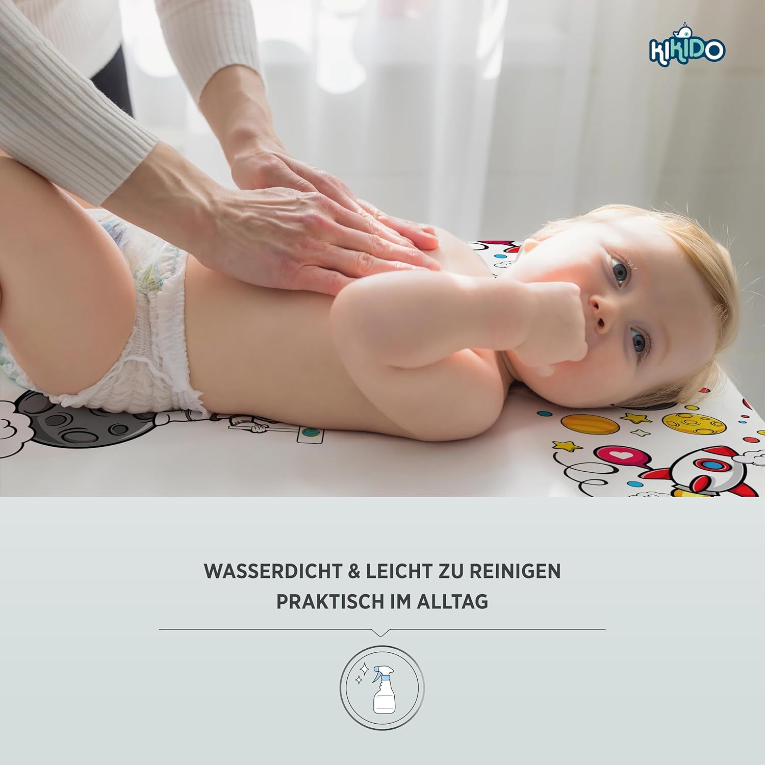Baby liegt auf Wickelauflage. Hände massieren Babybauch. Aufdruck: Rakete, Mond, Sterne.