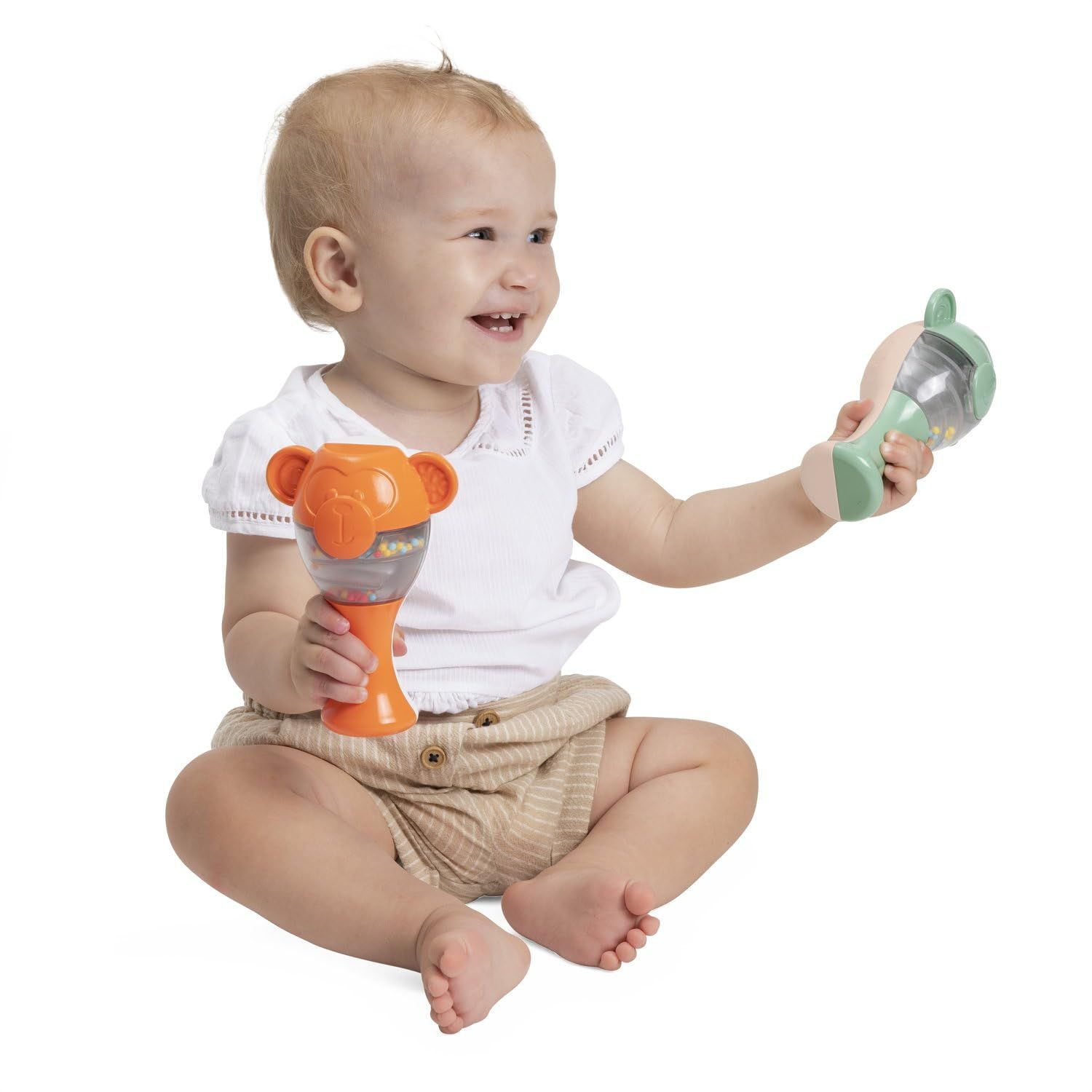 Ein Baby hält zwei bunte Affen-Rasseln, eine grüne und eine orange, in den Händen.