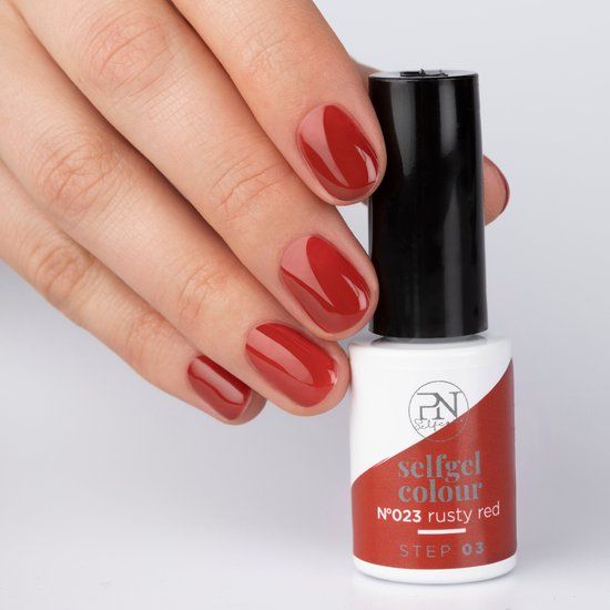 Hand mit lackierten Nägeln in Rostrot. Nagellackflasche daneben. Produktinformationen auf dem Etikett sichtbar. "N23 rusty red".