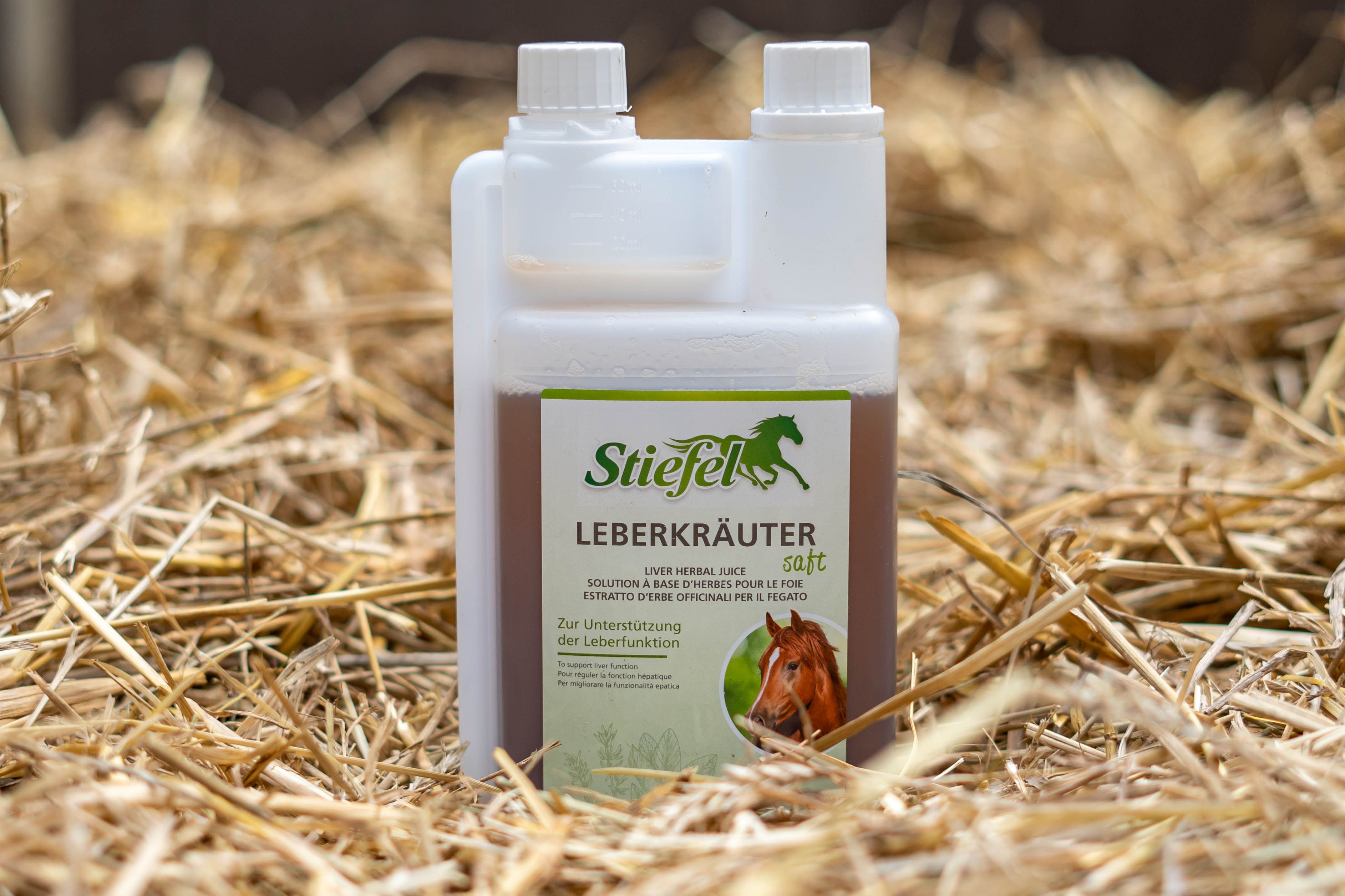 Flasche Stiefel Leberkräutersaft auf Stroh. Grünes Etikett mit Produktname, Logo und Text zur Leberfunktion.