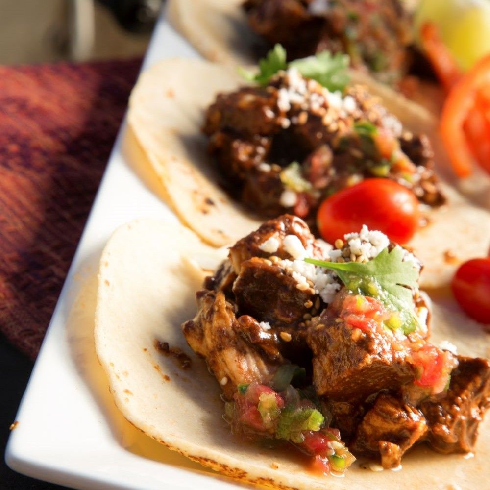 Tacos auf weißem Teller. Gefüllt mit Fleisch, Salsa und Käse. Tomaten und Koriander als Garnierung.