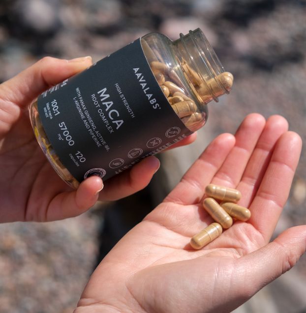 Hand hält Flasche mit Maca-Kapseln, einige Kapseln in der Handfläche.
