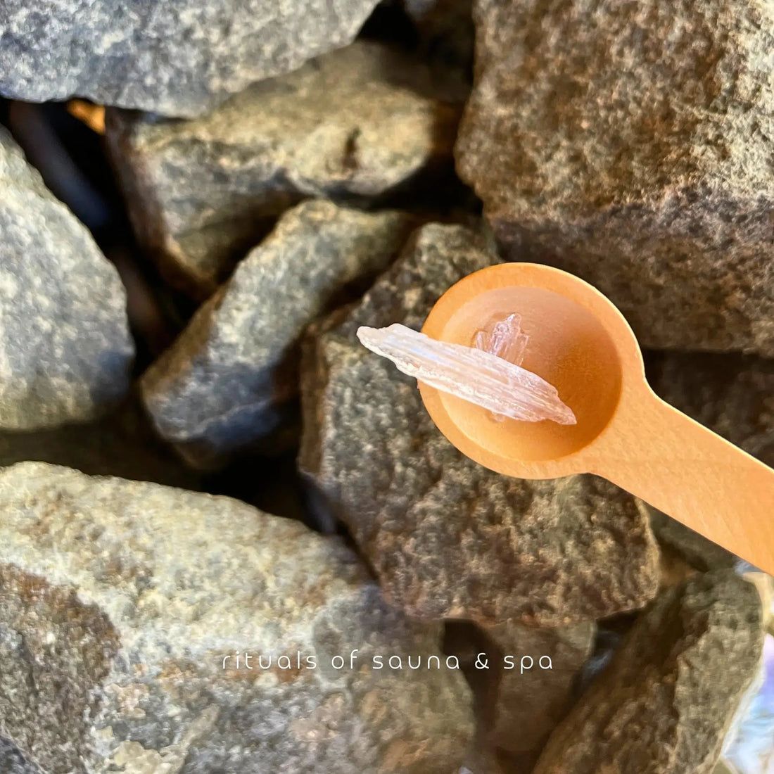 Holzlöffel mit Mentholkristall auf Saunasteinen. Aufschrift: rituals of sauna & spa.