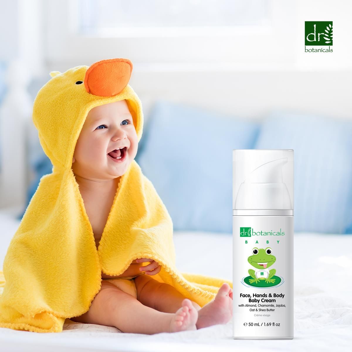 Lächelndes Baby in gelbem Frosch-Bademantel neben Dr. Botanicals Babycreme.