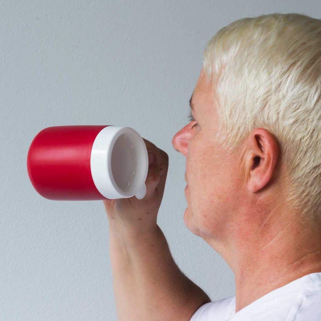 Person trinkt aus einem roten Becher mit weißem Deckel. Der Becher wird zum Mund geführt. Person im Profil.
