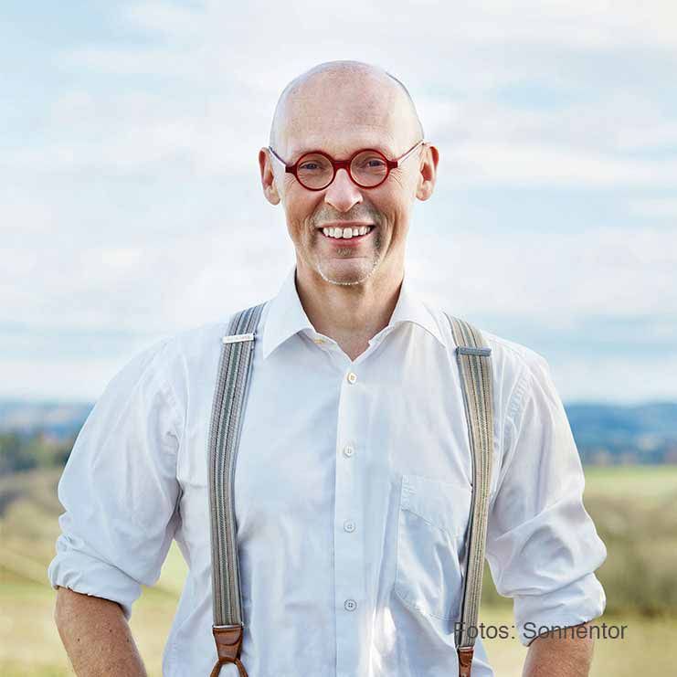 Ein Mann mit Brille und Hosenträgern lächelt in die Kamera.