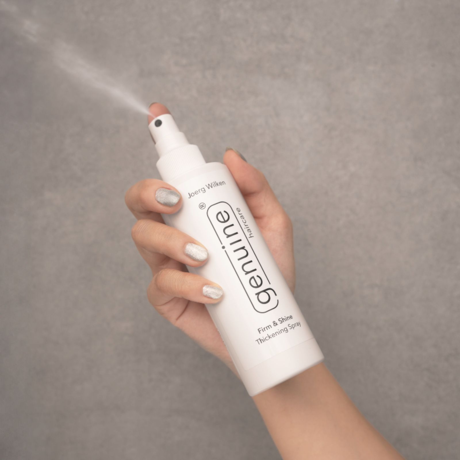 Weißes Spray in Hand, sprüht. Aufschrift: genuine haircare, Firm & Shine Thickening Spray.