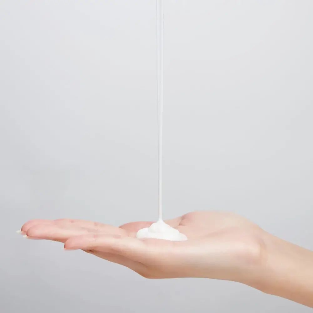 Weiße Creme fließt auf eine Hand. Hintergrund: weiß. Creme-Textur.