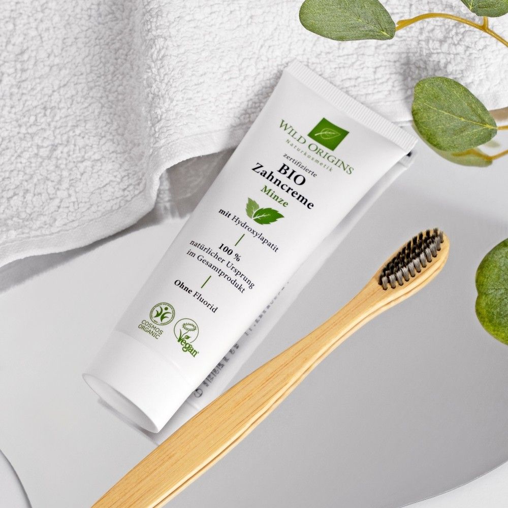 Zahncreme-Tube und Zahnbürste auf einer Oberfläche. Die Tube zeigt Schriftzug "Bio Zahncreme Minze".