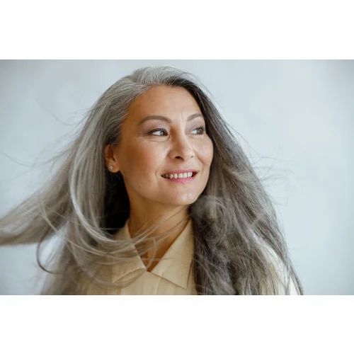 Porträt einer lächelnden, älteren Frau mit langen, grauen Haaren. Sie blickt zur Seite.