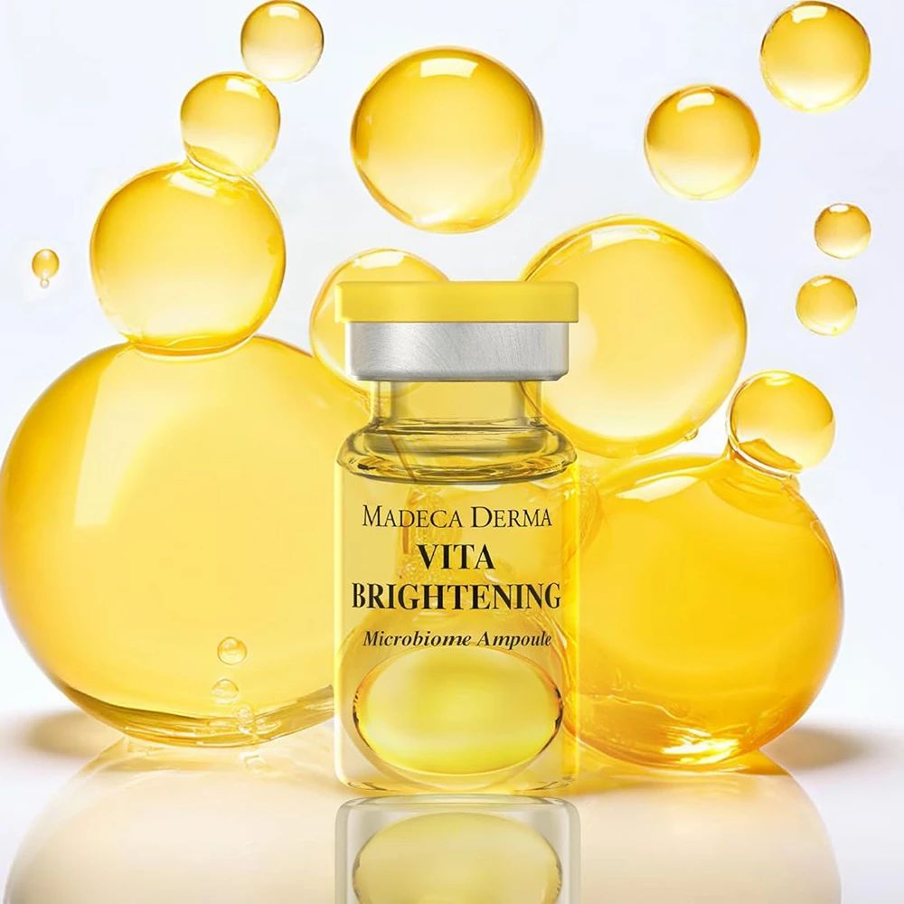 Glasampulle mit gelber Flüssigkeit. Beschriftung: MADECA DERMA VITA BRIGHTENING Microbiome Ampoule. Gelbe Blasen im Hintergrund.