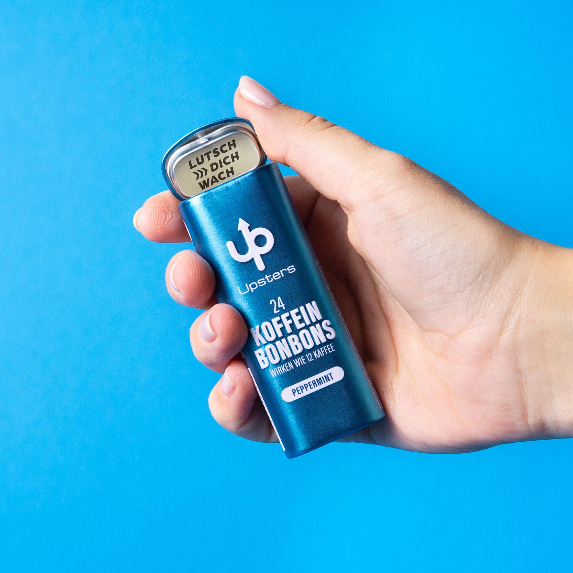 Hand hält blaue Dose mit Upsters Koffeinbonbons, Pfefferminze. Auf blauem Hintergrund.