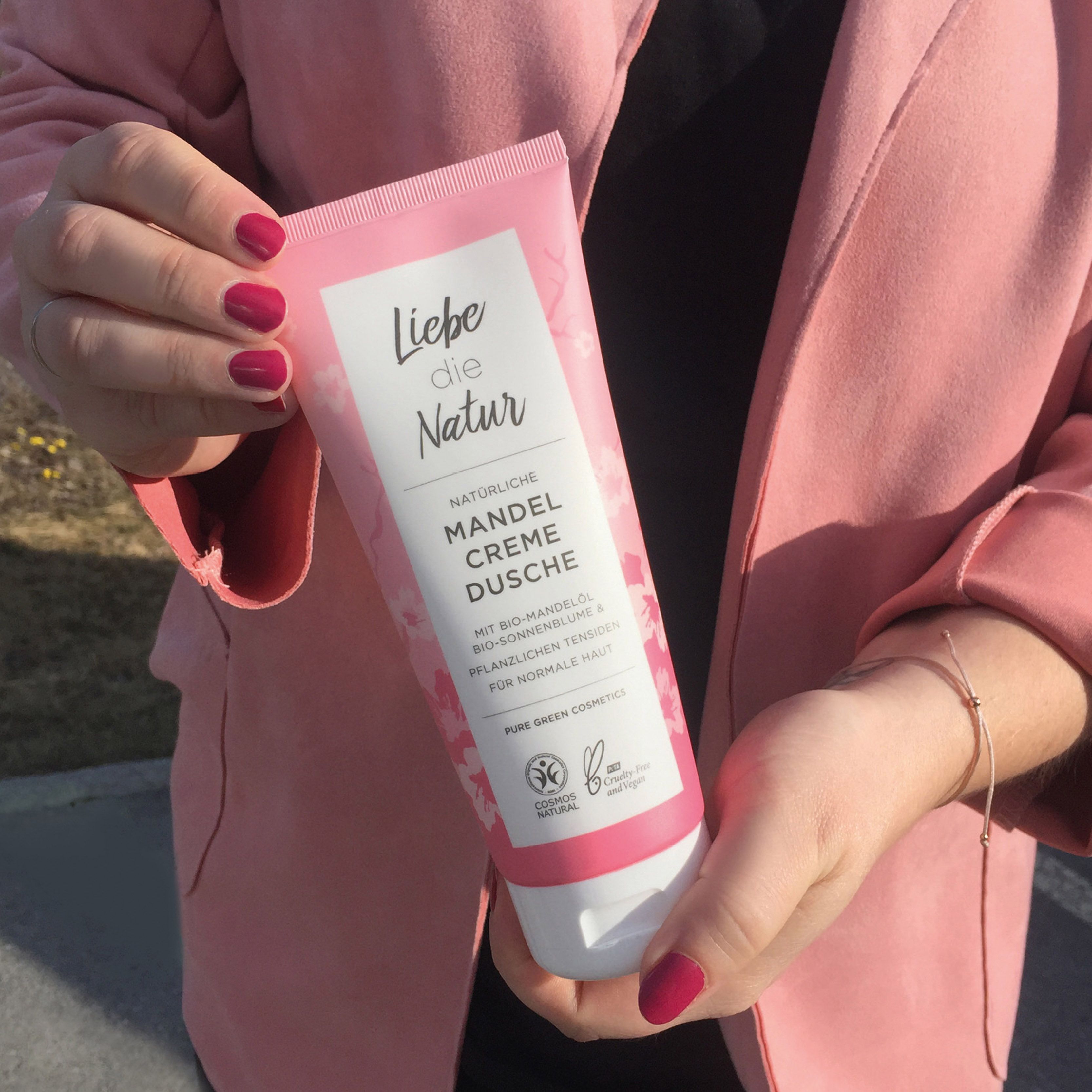 Rosa Tube mit weißem Verschluss. Aufschrift: Liebe die Natur, Mandel Creme Dusche. Vegan-Siegel.