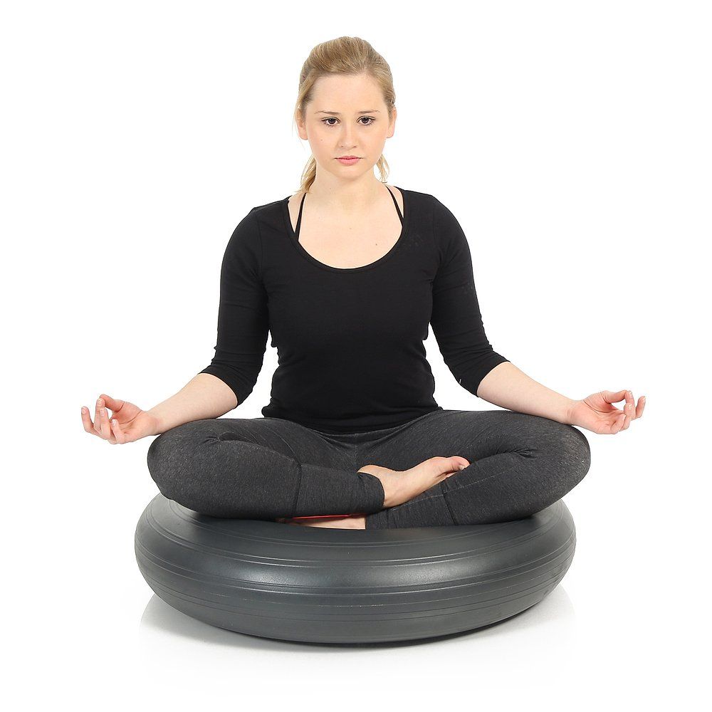 Person sitzt im Schneidersitz auf einem grauen, runden Ballkissen. Hände in Gebetshaltung.