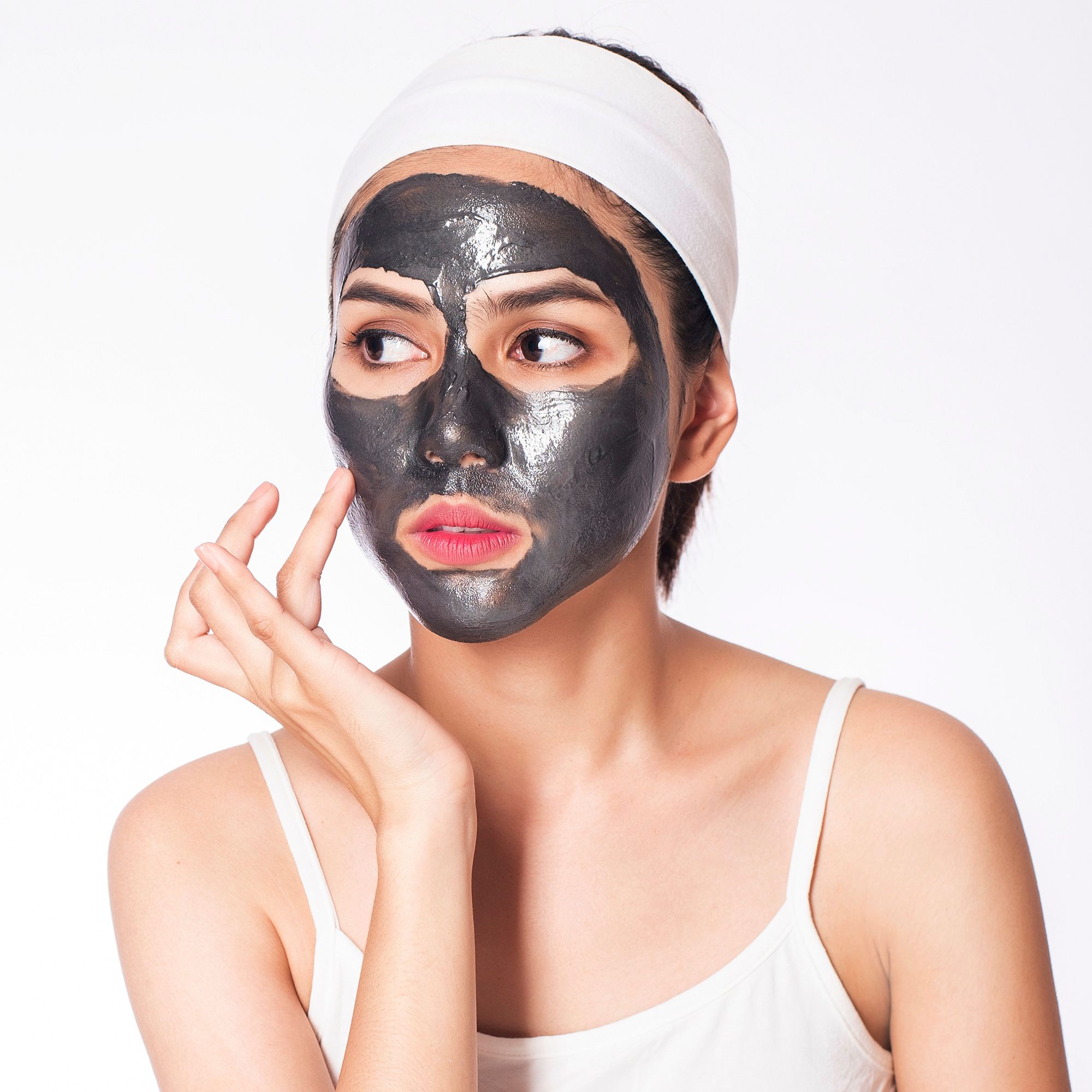 Frau mit Gesichtsmaske und Stirnband. Gesicht mit Maske bedeckt, berührt die Haut.
