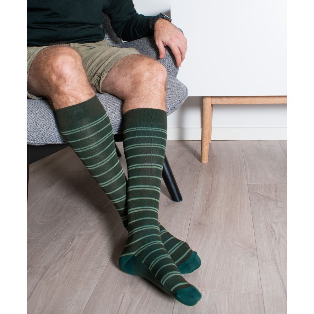 Person sitzt mit grünen Kniestrümpfen mit helleren Streifen. Dunkelgrüne Ferse und Zehenbereich. Blick von vorne.