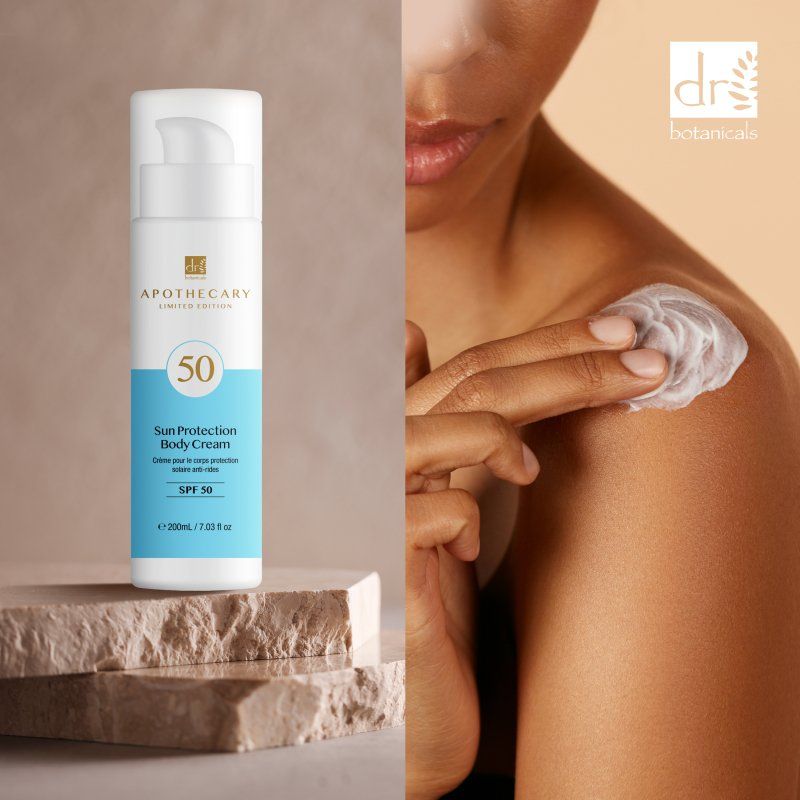 Körpercreme mit SPF 50. Weiße Flasche mit blauem Etikett. Person trägt Creme auf die Schulter auf.