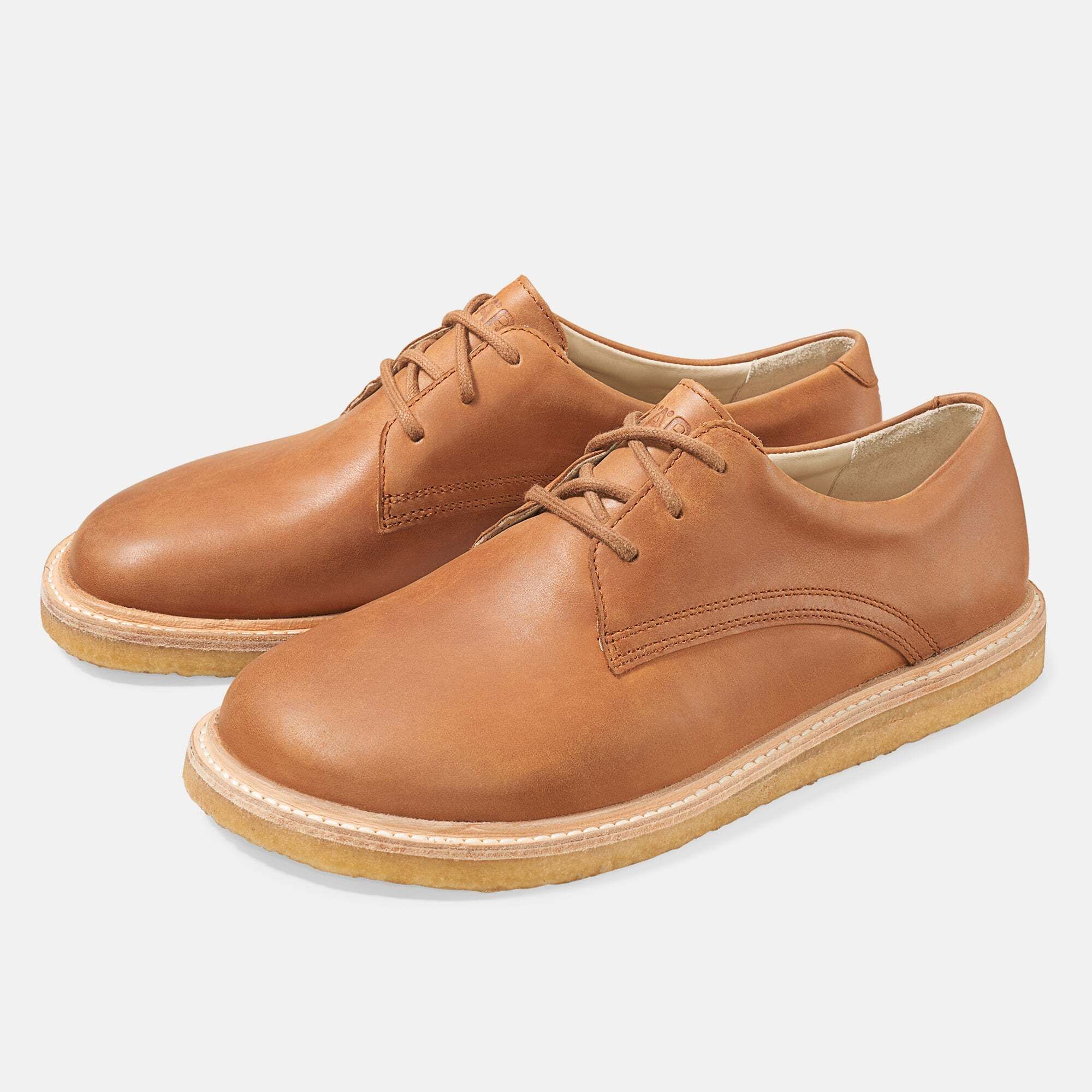 Zwei braune Lederschnürschuhe. Runde Zehen, helle Sohle. Schnürsenkel. Hellbraunes Leder.
