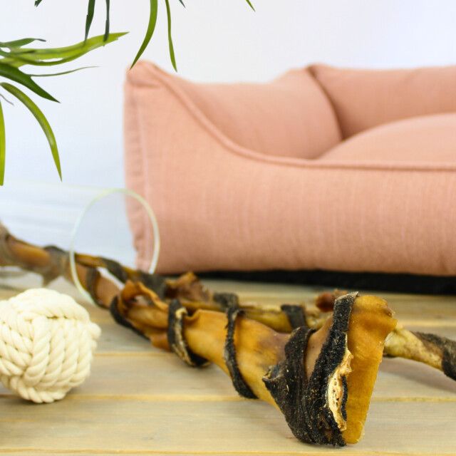 Lyra Pet Rinderkopfhautstangen mit Pansen neben einem Hundebett und einem Spielzeug. Auf Holzuntergrund.