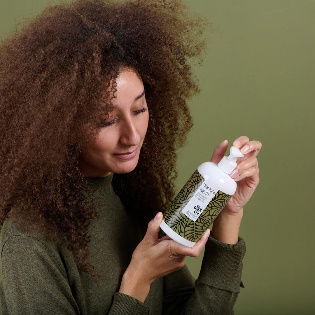 Frau hält Shampoo-Flasche. Weißes Fläschchen mit Pumpe, grünes Muster, Text: Tea Tree Oil.