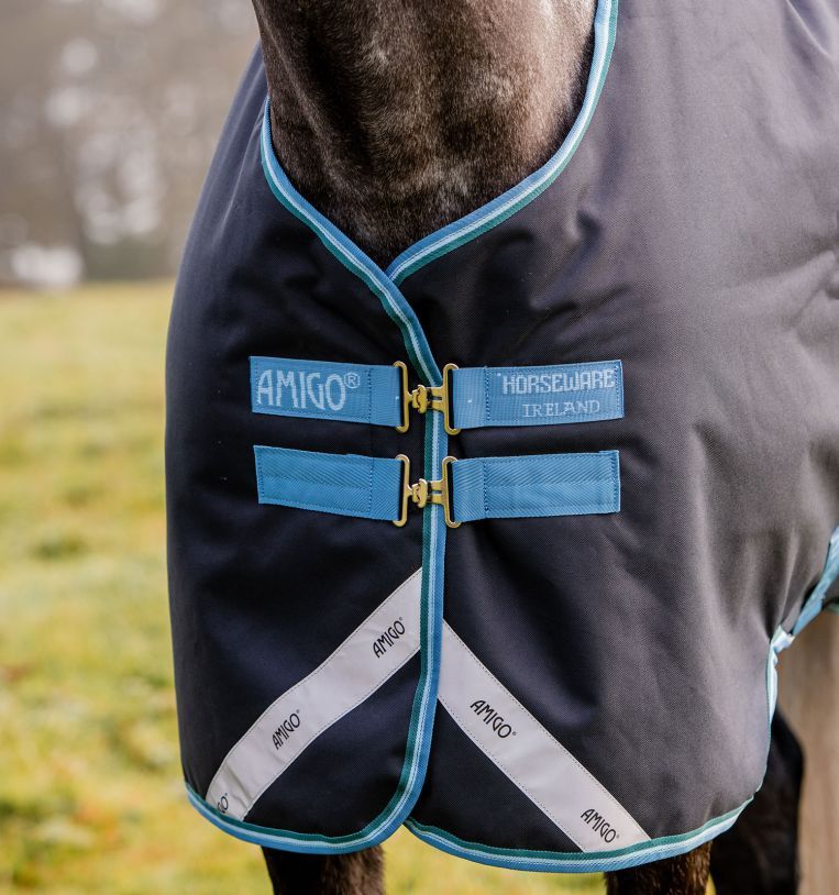 Nahaufnahme einer dunkelblauen Pferdedecke mit türkisfarbenen Rändern und Verschlüssen. Auf der Decke sind Logos von 'AMIGO' und 'HORSEWARE IRELAND' zu sehen.