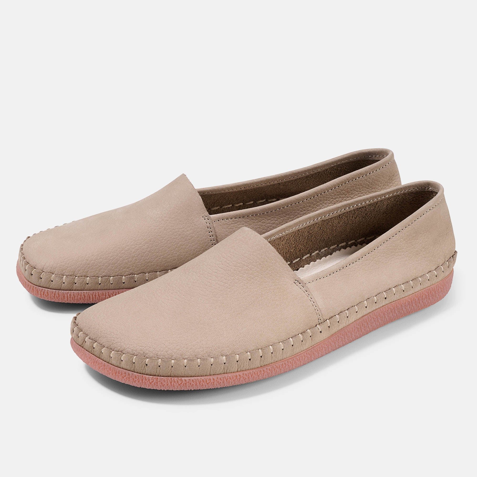 Zwei beigefarbene Unisex-Slipper mit roter Sohle. Sichtbare Nähte. Flache Form.