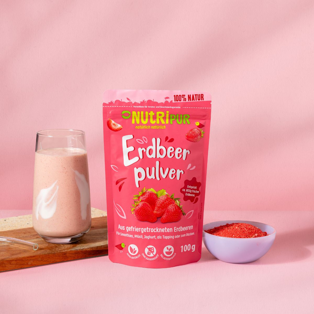 Rosa Beutel mit Erdbeerpulver, Glas mit Erdbeergetränk, Schale mit Pulver. Marke: NutriPur. Aufschrift: Erdbeerpulver, 100g.