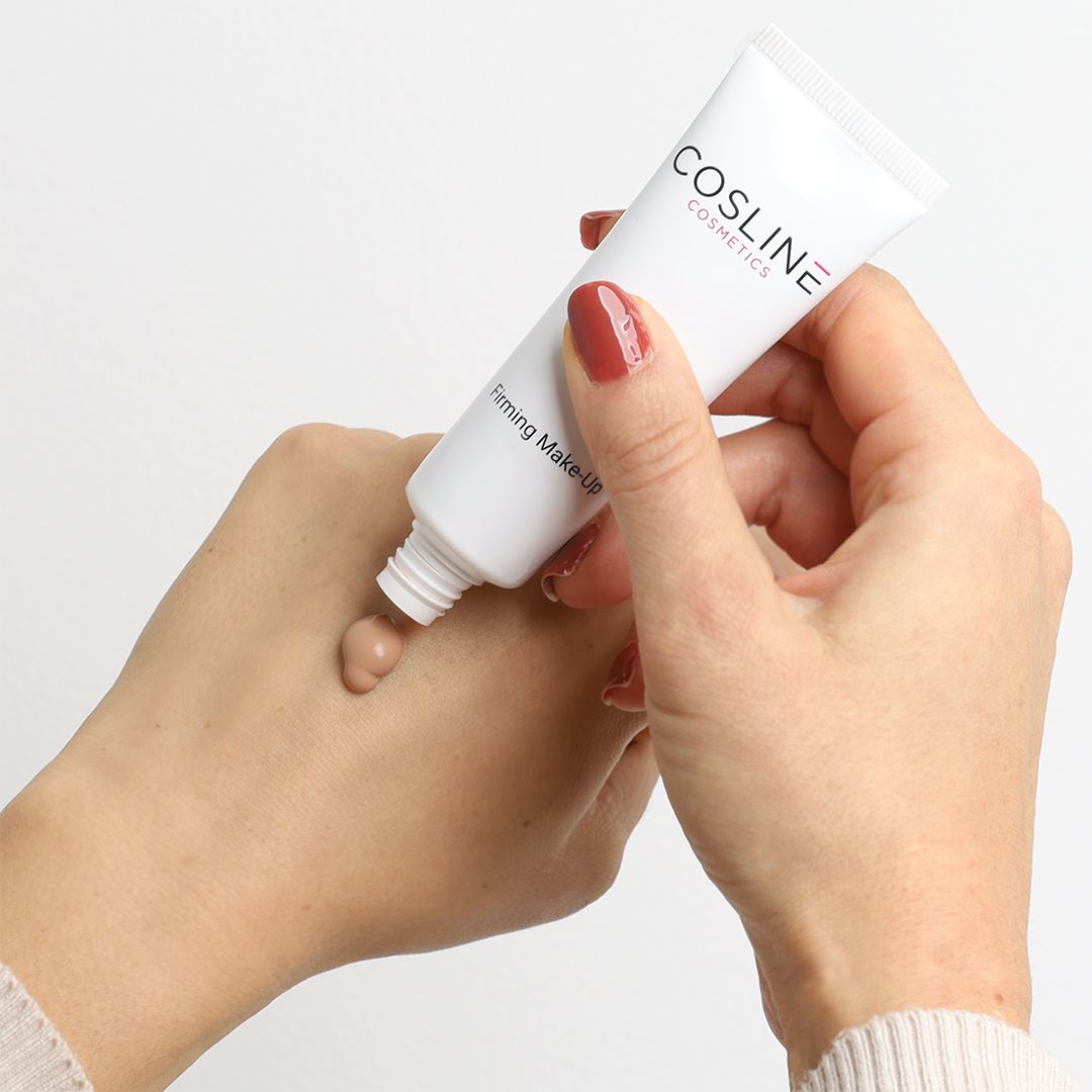 Hände drücken Cosline Firming Make Up aus einer Tube. Creme-Farbe. Hintergrund weiß.