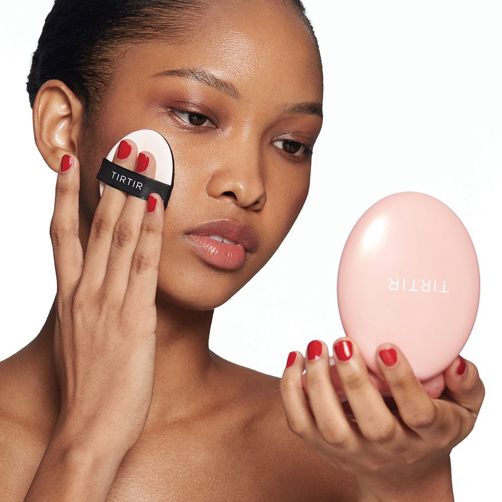 Person, die einen Make-up-Schwamm auf das Gesicht aufträgt. Rosa Kompakt-Make-up-Behälter mit Marke TIRTIR.