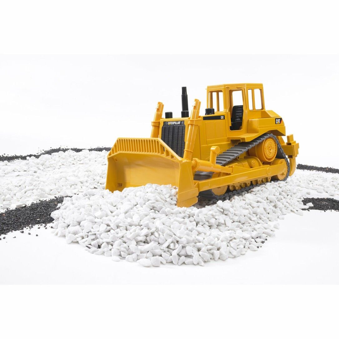 Gelber Bruder Cat® Bulldozer auf weißen Steinen. Raupenfahrwerk, Schaufel, Kabine. Schwarze Steine als Weg.
