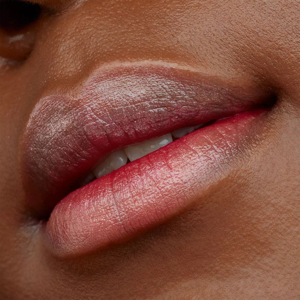 Nahaufnahme von Lippen, die mit einem roten Lippenstift geschminkt sind. Die Lippen sind glänzend und die Farbe variiert von rot bis rosa.