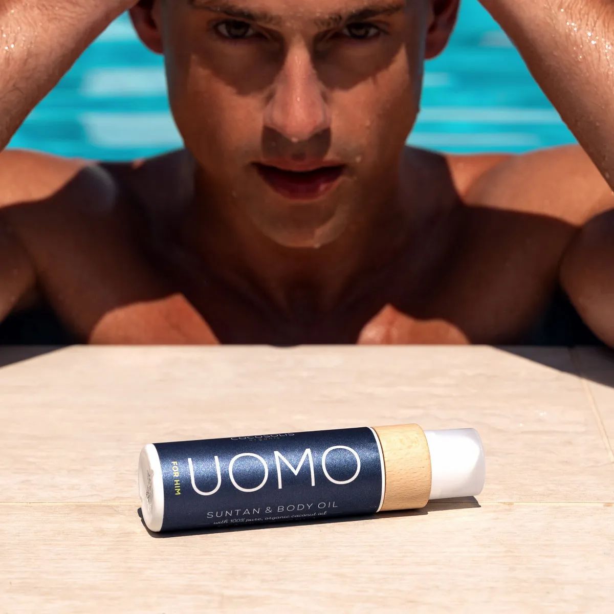 Mann im Pool blickt auf eine Flasche COCOSOLIS UOMO Bräunungsöl.