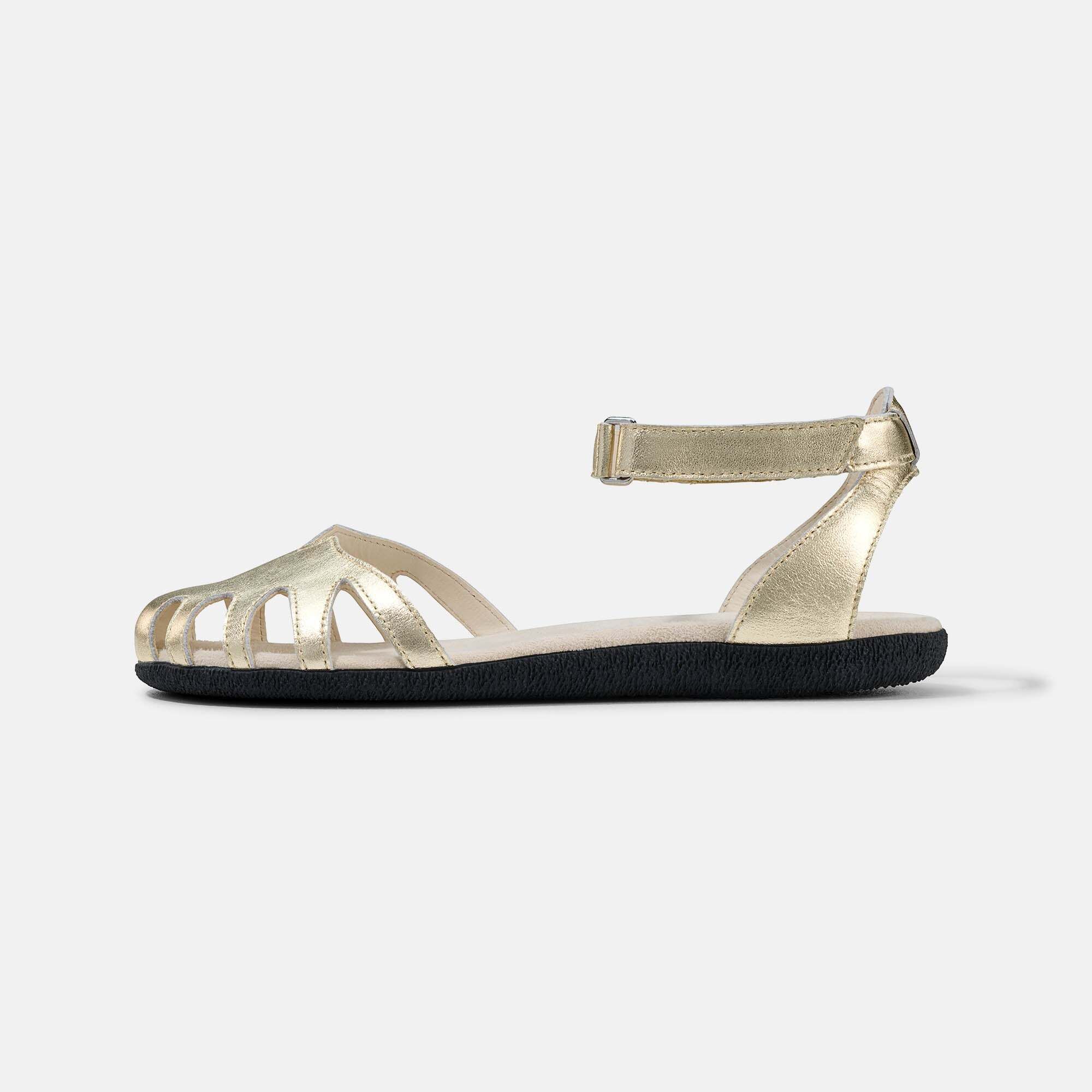 Seitenansicht einer goldenen Damen-Sandale mit verstellbarem Knöchelriemen und flacher Sohle.