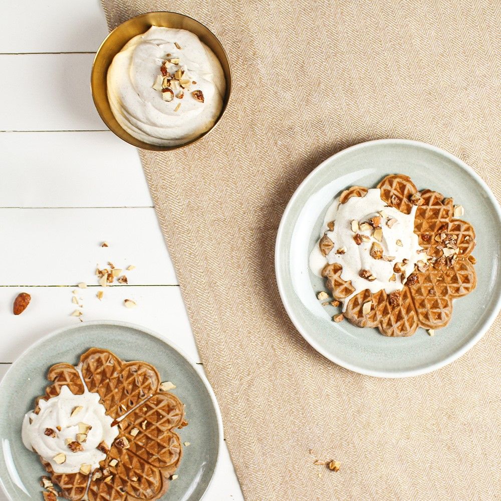 Waffeln auf Tellern mit Sahne und Nüssen. Eine Schüssel mit Sahne und Nüssen. Auf hellem Untergrund.
