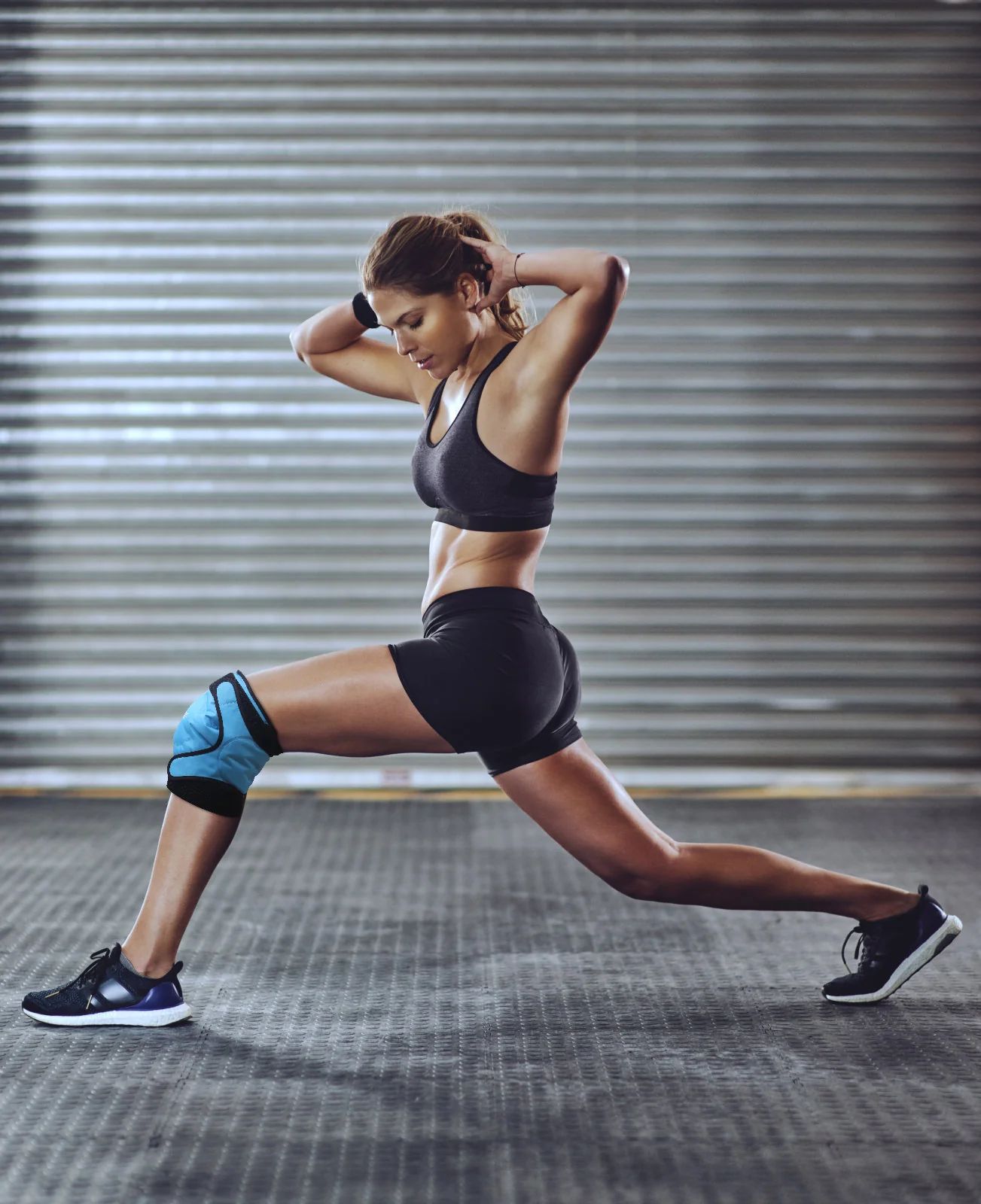 Frau in Ausfallschrittposition mit blauer Knie-Kühlmanschette im Fitnessstudio.