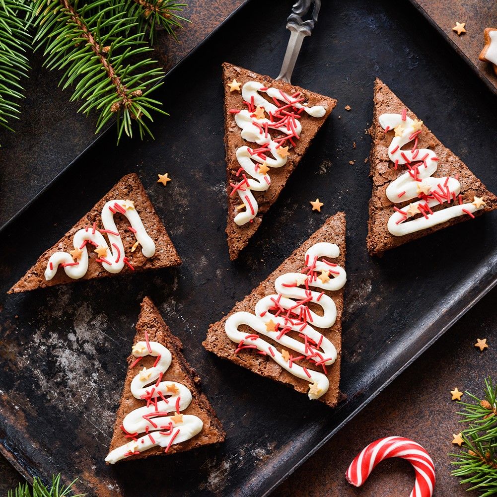Fünf dreieckige Brownies, weihnachtlich verziert. Auf schwarzem Tablett. Dekoration: Sterne, Zweige, Zuckerstange.
