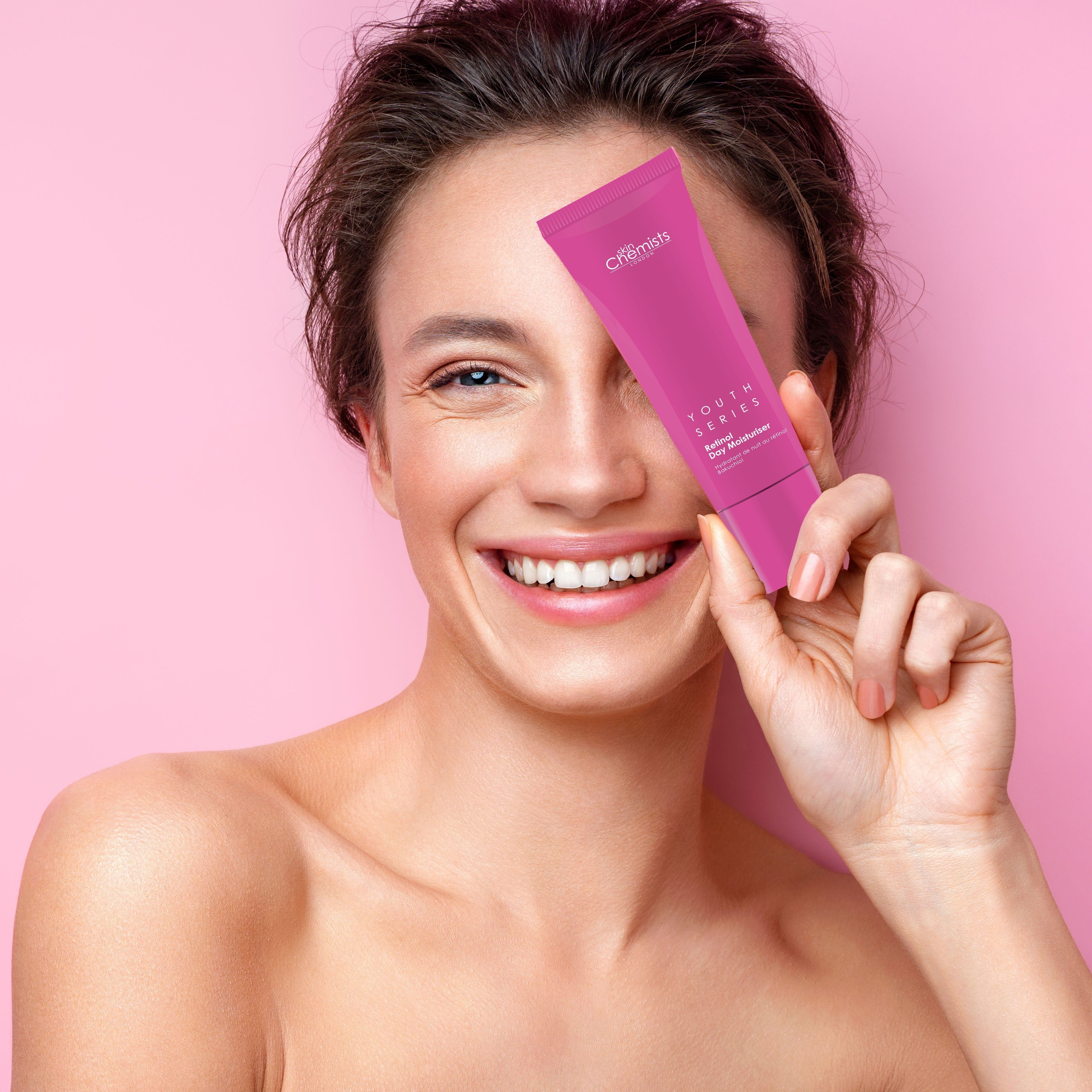 Frau hält rosa Tube vor dem Auge. Aufschrift: Youth Series, Retinol Day Moisturiser. Marke: skinChemists.