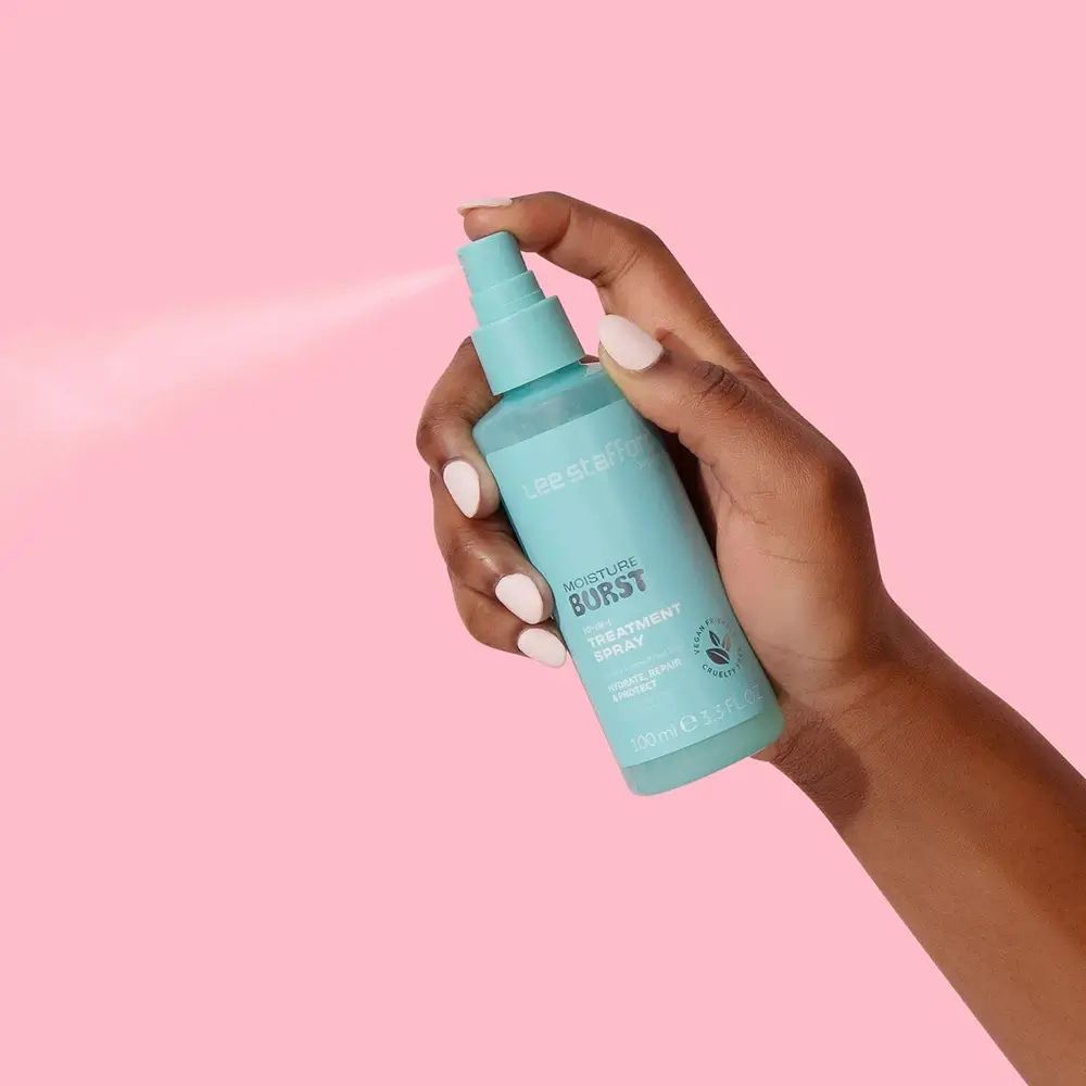 Hand hält türkisfarbene Sprühflasche. Aufschrift: Lee Stafford, Moisture Burst, 10-in-1 Treatment Spray. Sprühnebel sichtbar.
