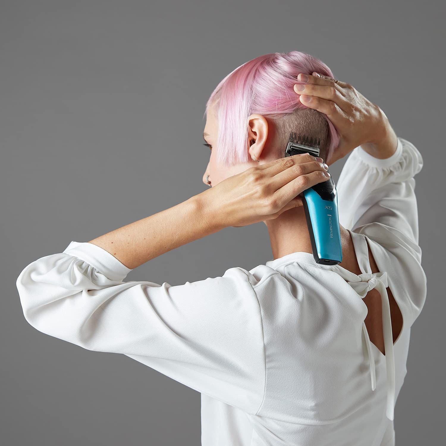 Person schneidet Haare mit blau-schwarzem Haarschneider. Frau mit pinken Haaren.